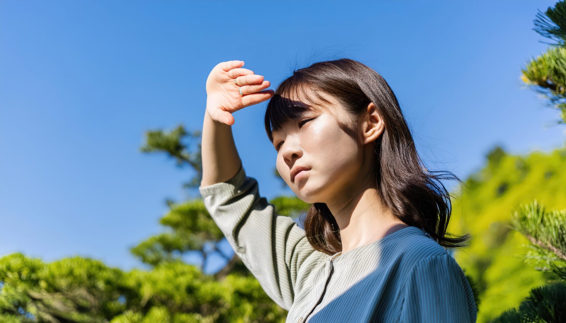 緑に囲まれて日差しを遮る女性