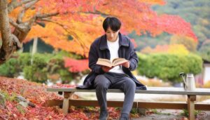 秋の紅葉の中で読書を楽しむ若い男性