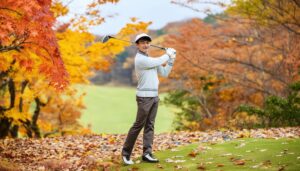 紅葉のゴルフ場でスイングをする男性