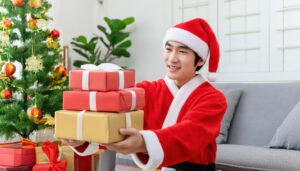 サンタ帽をかぶったプレゼントを渡す笑顔の男性（室内）