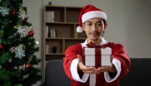 サンタ帽をかぶった男性がプレゼントを差し出す（室内）
