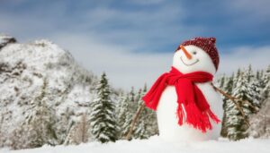 雪山を背景に立つ赤いマフラーの雪だるま