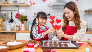 子供と一緒にハート型の飾りを作るエプロン姿の女性