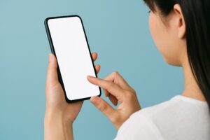 青背景でスマートフォンを操作する女性（背面）