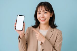 スマホを見せるスーツ女性（指差し・ブルーバック）