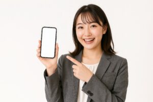 スマホを指差すビジネスウーマン（白背景・グレースーツ）