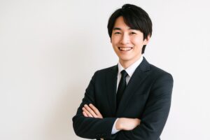 腕を組んで笑顔を見せるスーツ姿の男性（白背景）