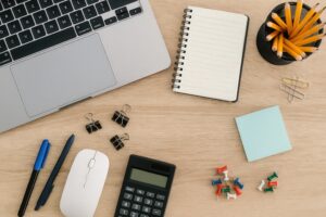 木目調デスクに広がるオフィス用品とノートパソコン