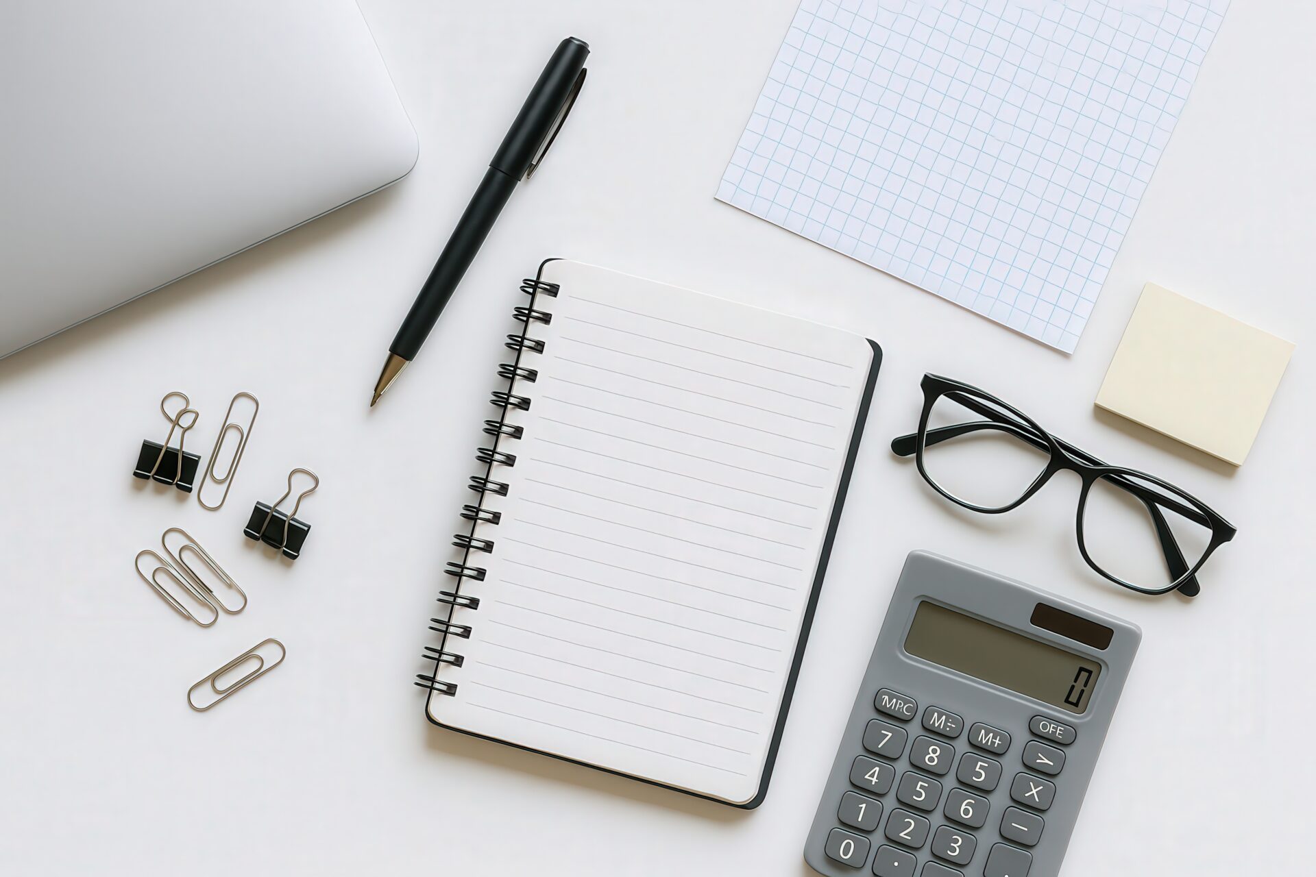 白背景のデスクに並ぶノートパソコンと文房具