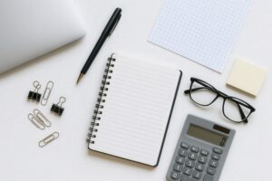 白背景のデスクに並ぶノートパソコンと文房具