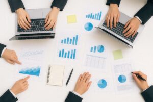 白いデスクに並ぶノートパソコンと円グラフ資料