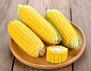 木製プレートに並んだ皮付きとカットしたトウモロコシ