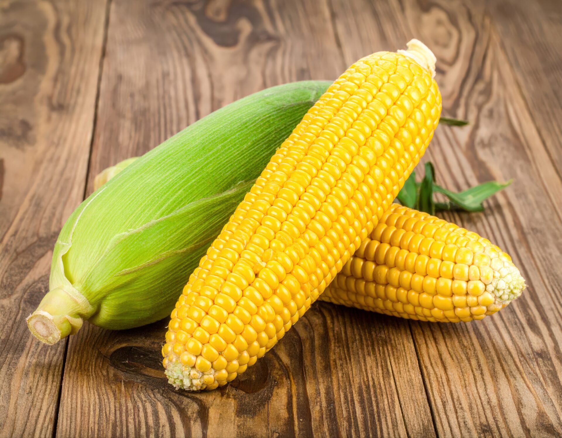 皮付きとむき出しのトウモロコシ3本を木製テーブルの上に置いた