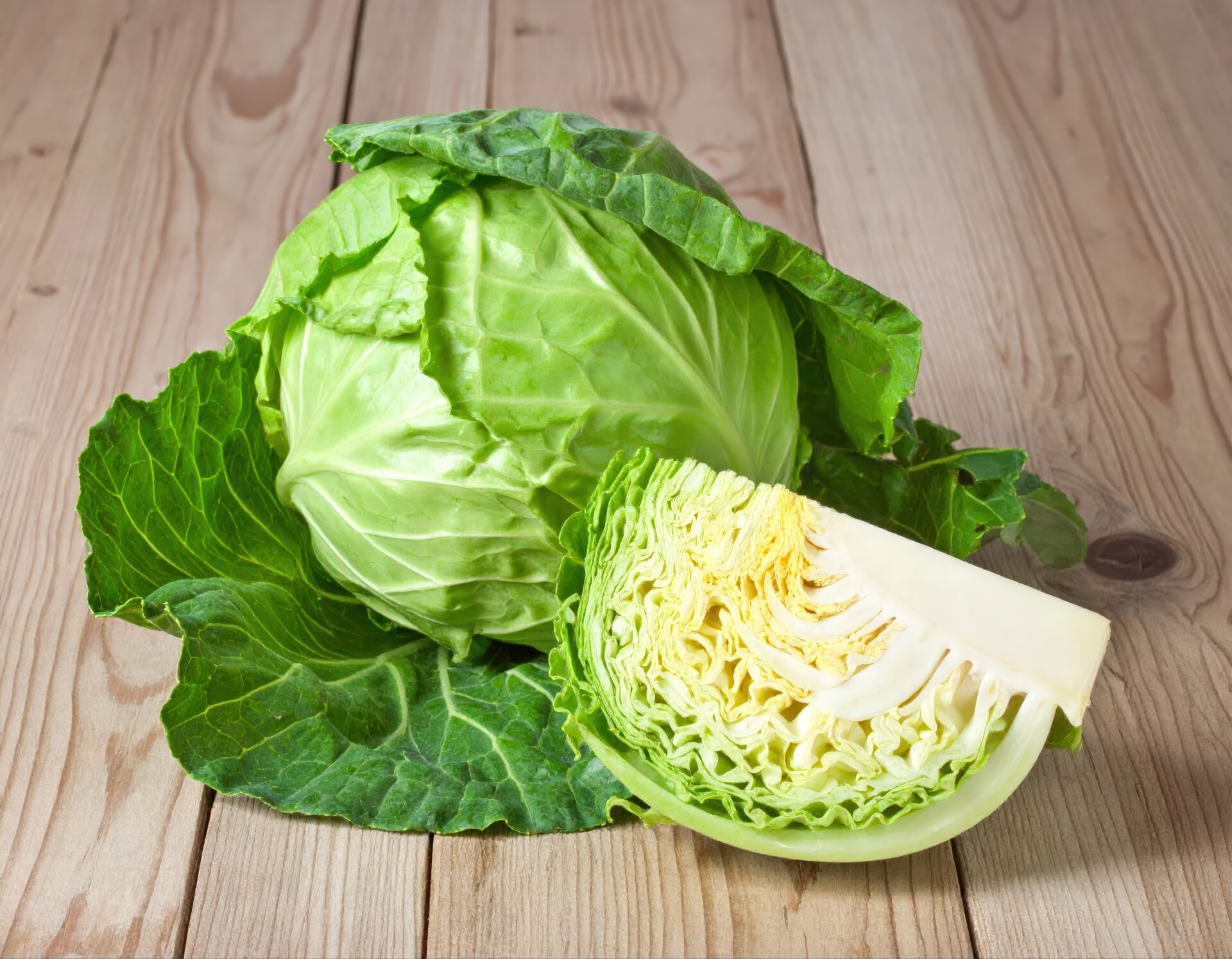 木のテーブルに丸ごとのキャベツとカットキャベツ