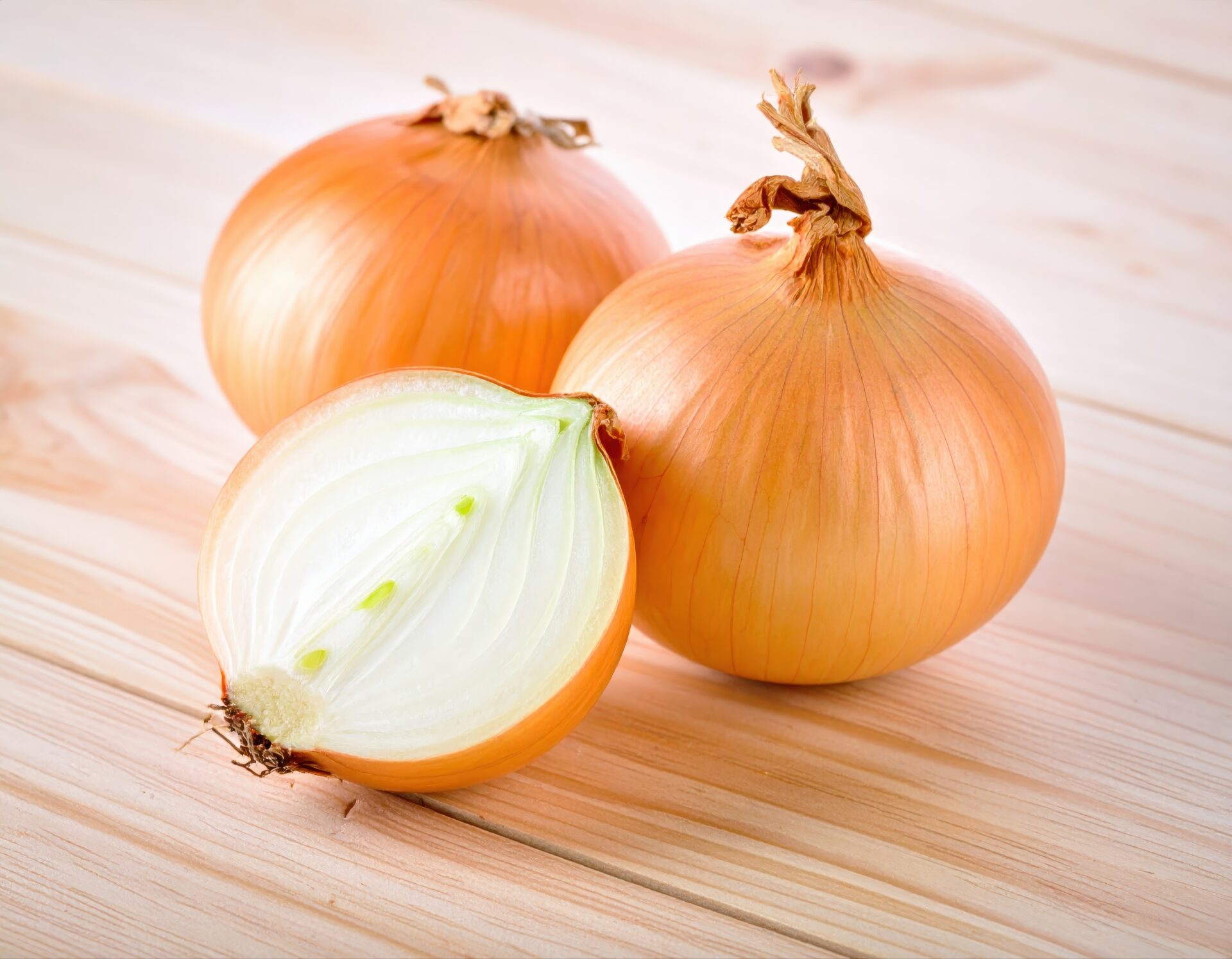 木のテーブルに置かれた丸ごとの玉ねぎと半分にカットした玉ねぎ