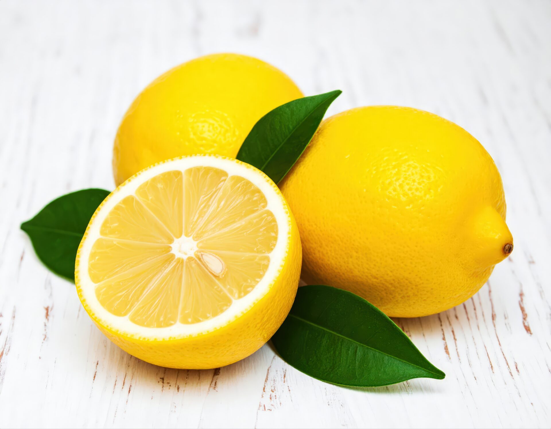白い木製テーブルに置かれたカットレモンと丸ごとのレモン