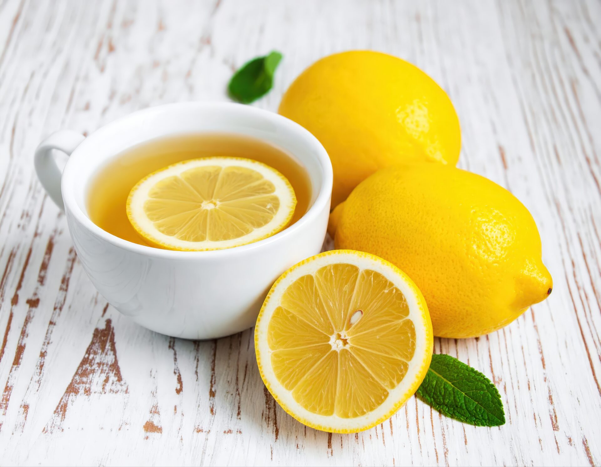 白いカップのレモンティーとカットレモンとミント