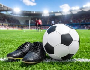 スタジアムの芝生に置かれたサッカーボールと黒いシューズ