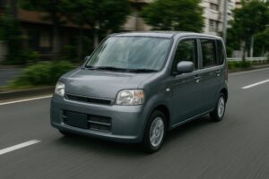 緑の街路を走るグレーの軽自動車