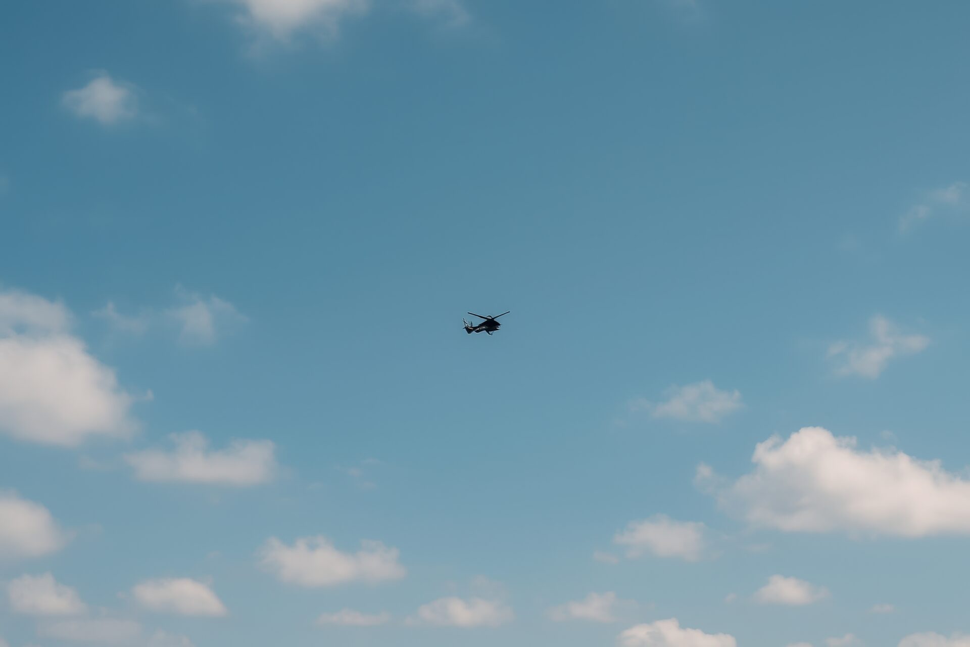 青空を飛行するシルエットの軍用ヘリコプター