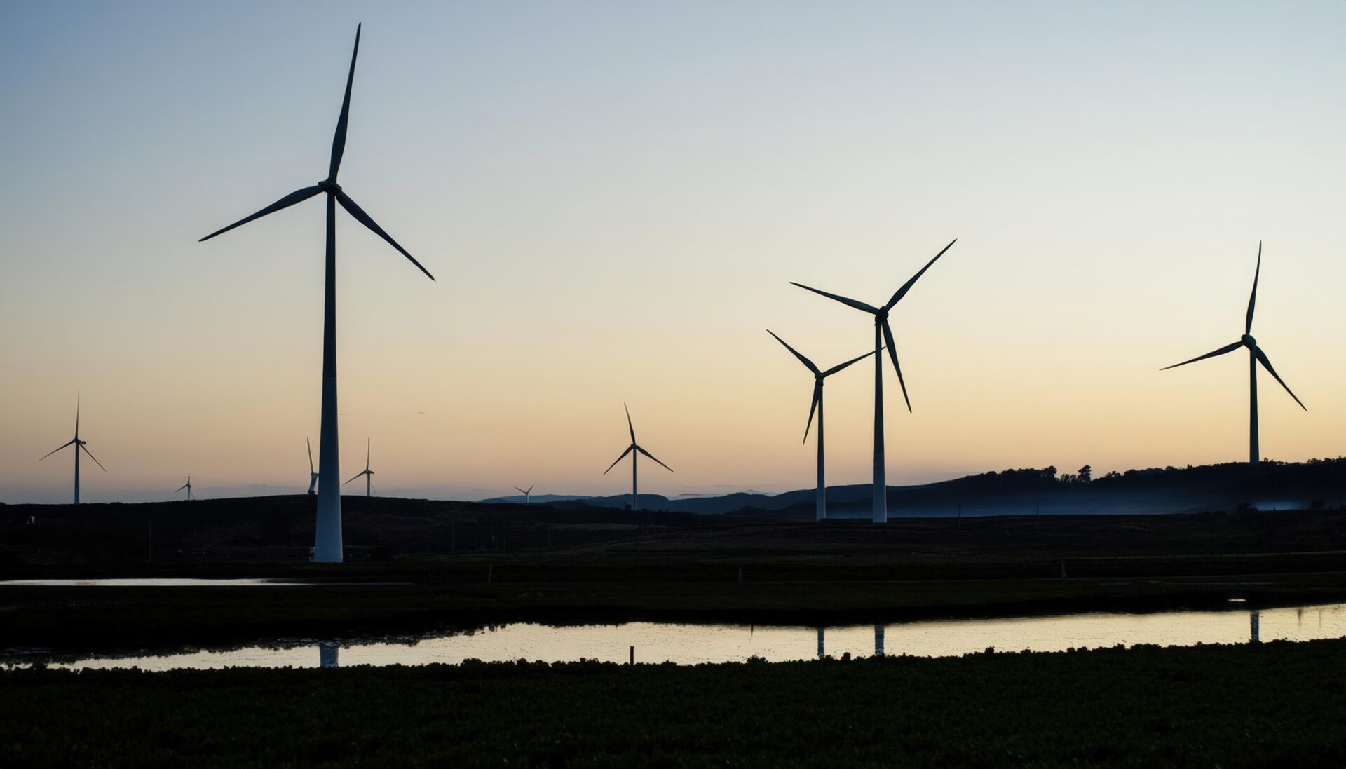 夕暮れ時の風力発電所と静かな水辺