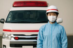 赤いサイレンカーの前に立つ救急救命士
