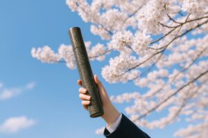 春の桜と空に向かって卒業証書を掲げる手元