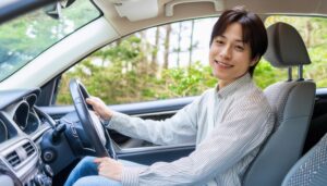 車を運転中の男性（白いシャツ・自然豊かな背景）