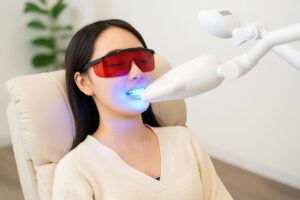 赤い保護メガネをかけてホワイトニングを受ける女性
