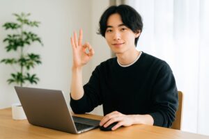 ノートパソコンの前でOKサインを見せる男性