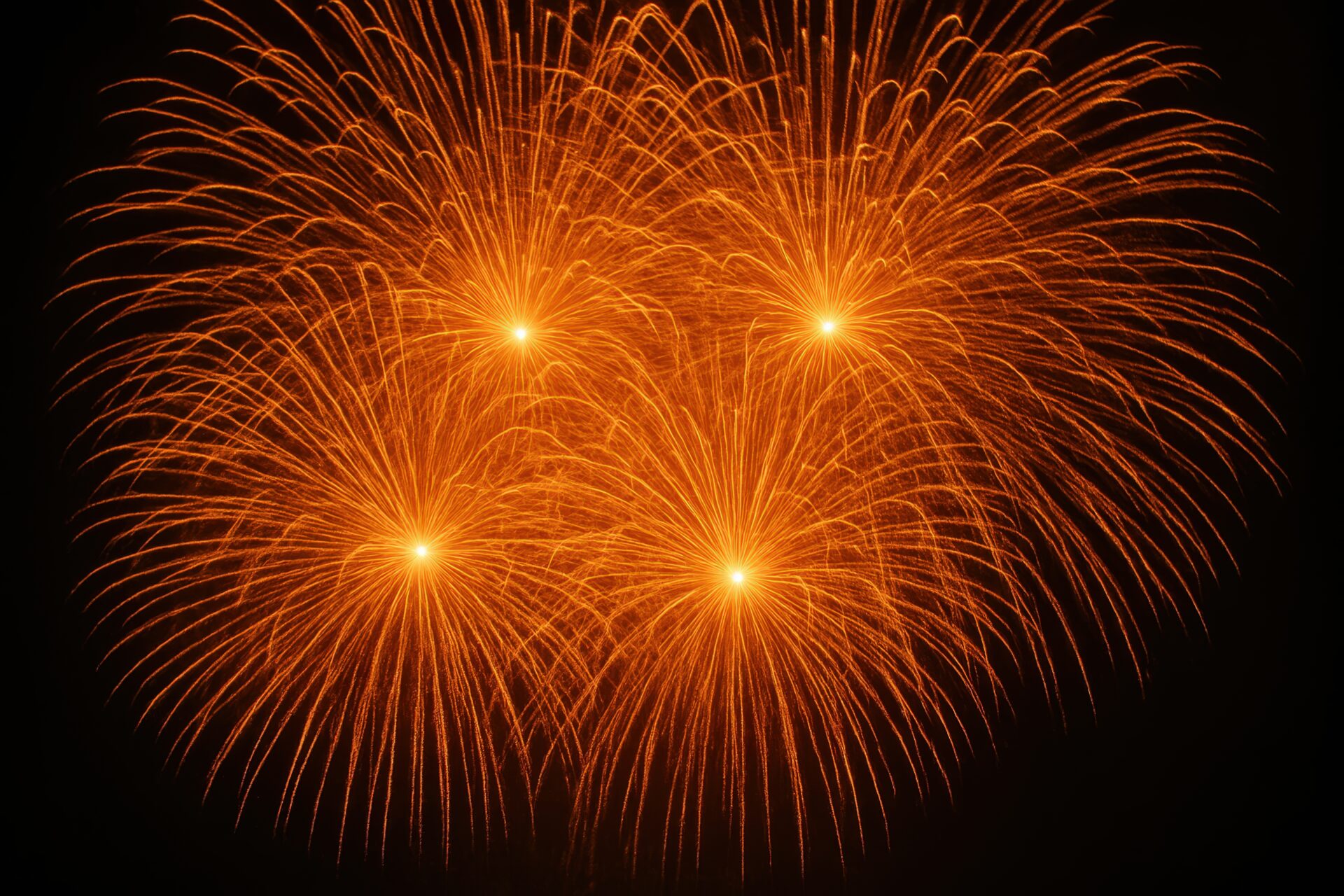 鮮やかな橙色の花火が4発開く夜空