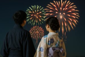 浴衣姿の男女が並んで夜空の花火を見る様子