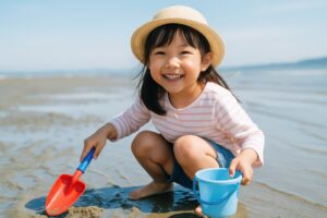 砂浜でバケツとスコップを持ち笑顔の女の子