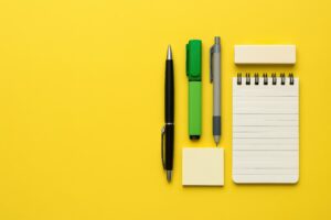 黄色背景に映える文房具とノートの平置き構図