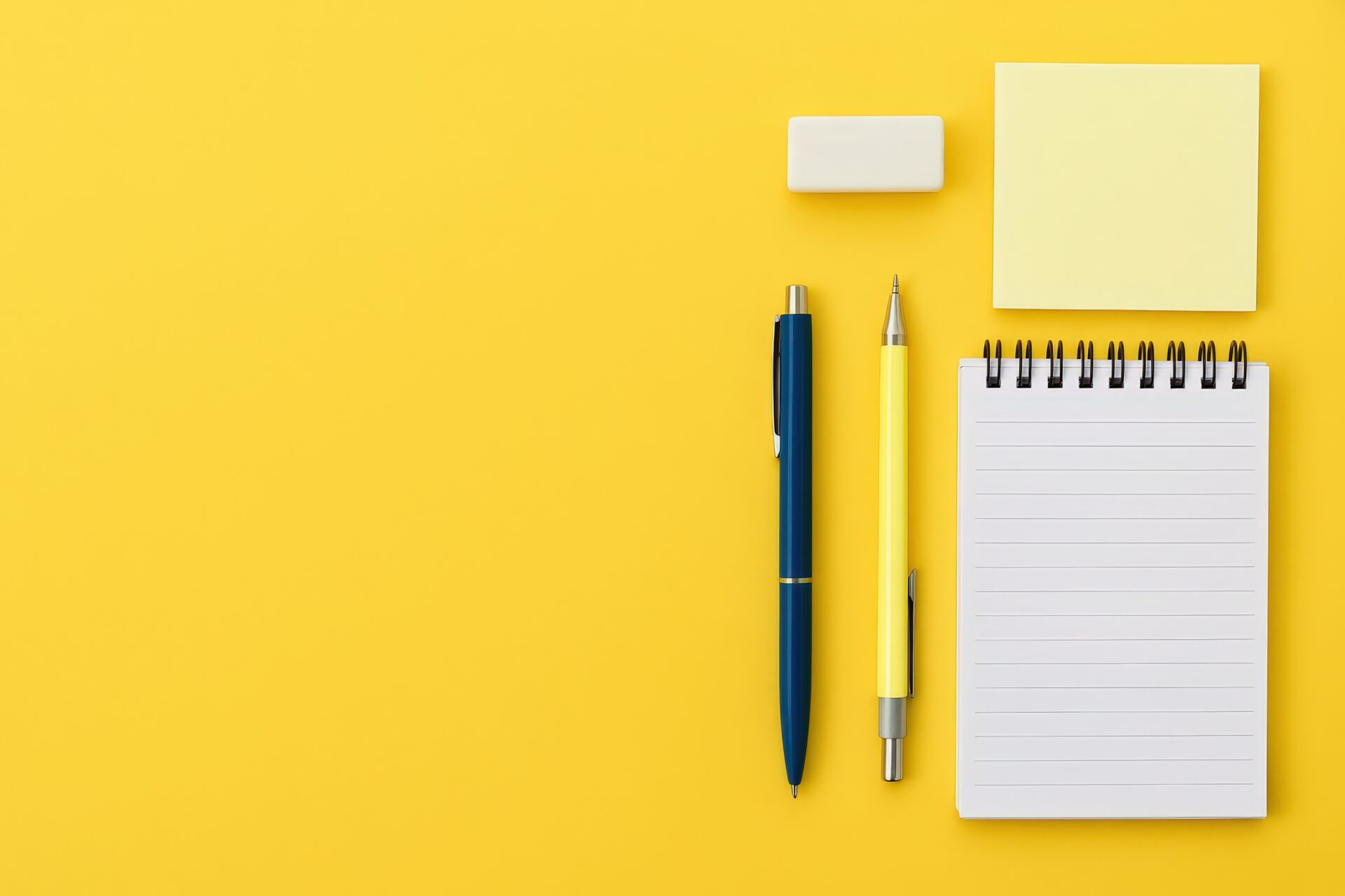 黄色背景に配置されたペンとノートと付箋