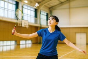 シャトルを狙ってバドミントンラケットを構える女子学生