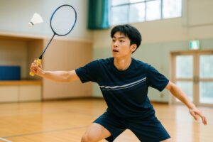 バドミントンの試合でシャトルを狙う男子学生