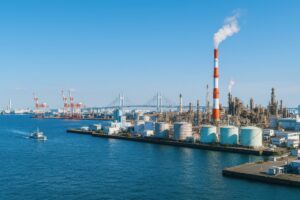 煙突から煙が上がる石油コンビナートと港湾クレーンのある風景