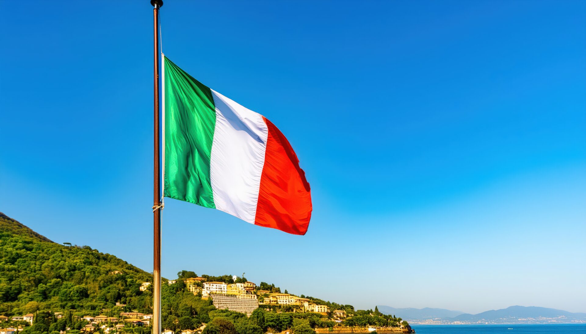 青空と山を背景に掲げられたイタリア国旗