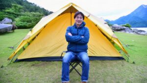 キャンプ場で黄色いテントの前に座る男性