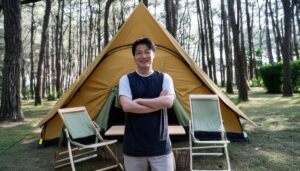 森の中でテントの前に立つ笑顔の男性