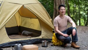 キャンプ場で食器を置いたテントの横に座る男性