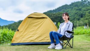 キャンプ場で黄色いテントの横に座る女性