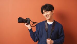 カメラを持って笑顔の男性（オレンジ背景）