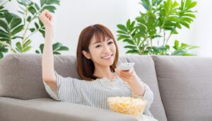 ソファでポップコーンを食べながらテレビを見る女性