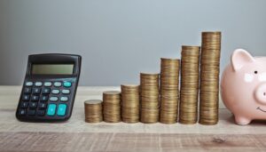 グレーの背景に並ぶ電卓とコインと貯金箱