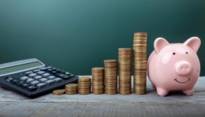 緑背景に並ぶピンクの貯金箱と硬貨と電卓