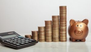 白背景に並ぶブロンズ色の貯金箱と硬貨と電卓