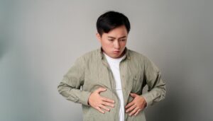 グレー背景でお腹を押さえる男性