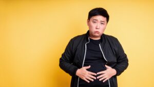 黄色い背景でお腹を押さえる男性